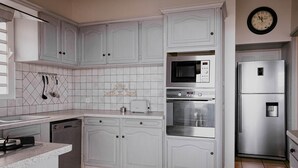 A kitchen with white cabinets, a microwave, an oven, a refrigerator, and a clock on the wall. - T3 Pisicine Chauffée et Privative (Saint-Leu)