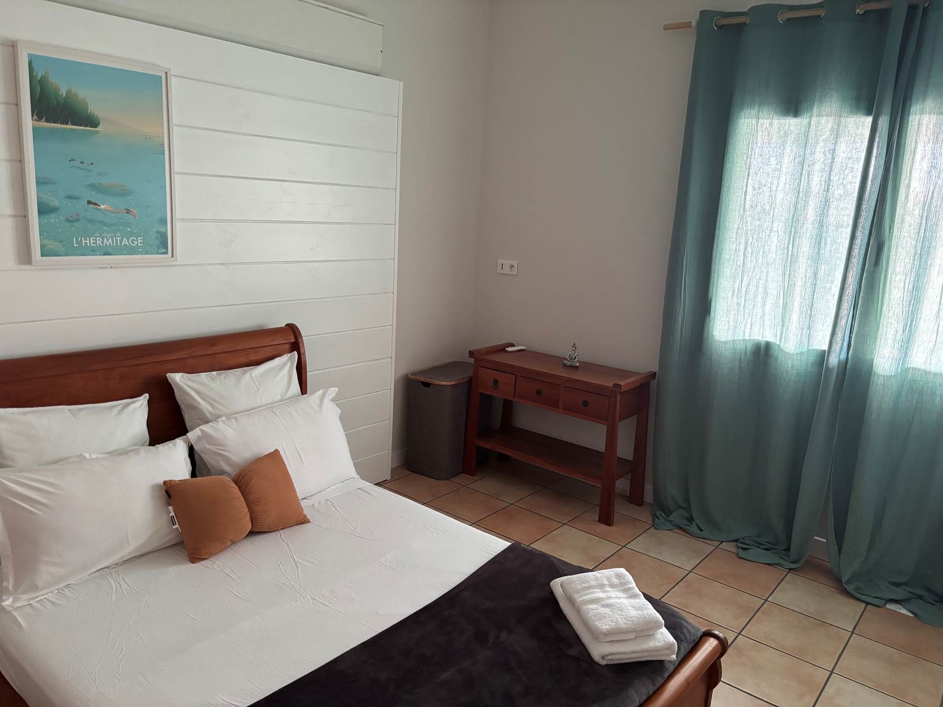 Une chambre à coucher avec un lit, des oreillers, une table de chevet, un bureau, une poubelle et une fenêtre avec des rideaux.