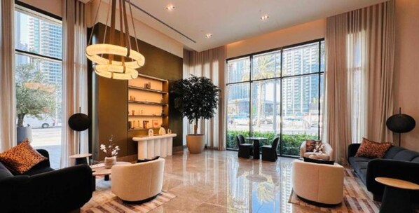 A spacious lobby with a modern chandelier, a large potted plant, and a seating area with sofas and a coffee table.