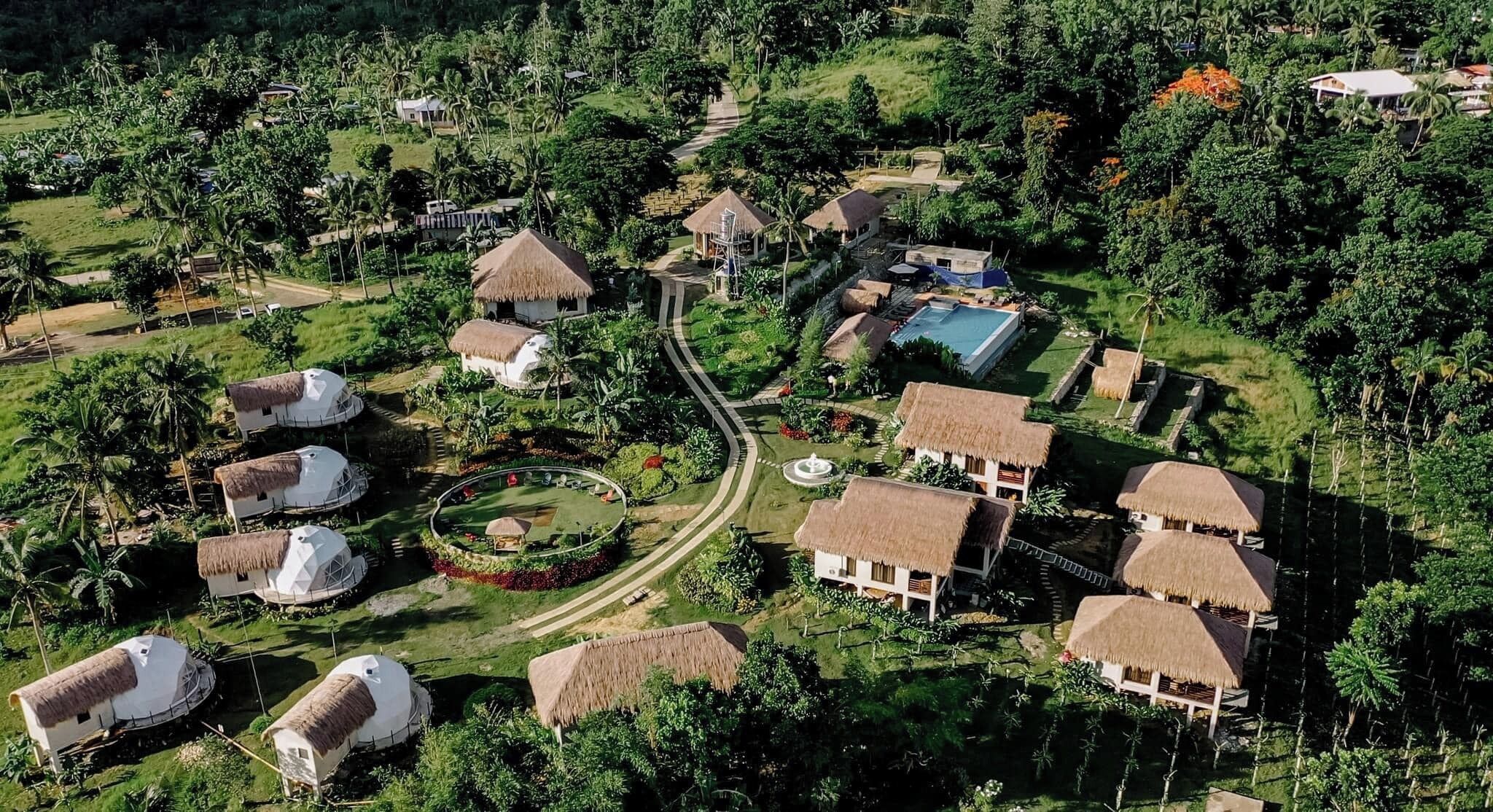 Vue aérienne d’un complexe hôtelier doté de bungalows aux toits de chaume, d’une piscine et d’une végétation luxuriante.