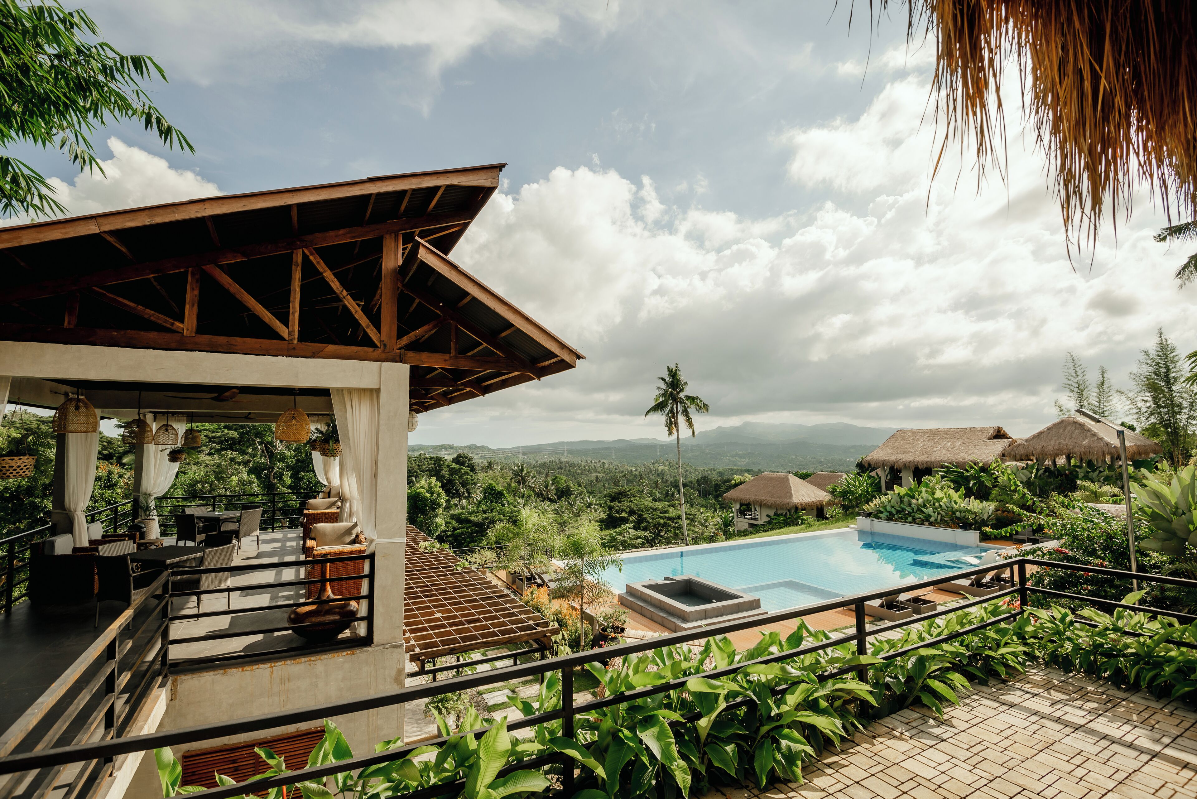 A pool area with a view of the mountains, a covered seating area, and lush greenery.