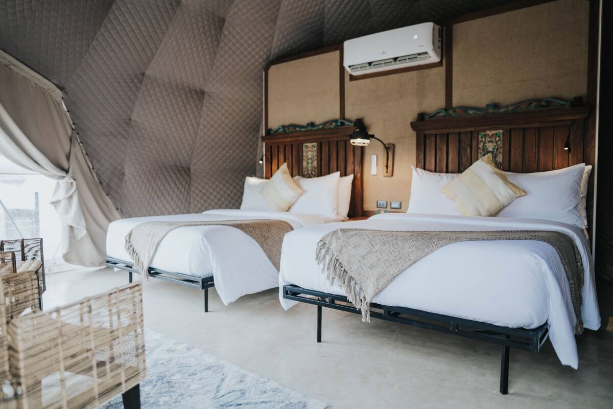 Una habitación acogedora con dos camas, un cabecero de madera, una cesta tejida y un ventilador de techo.