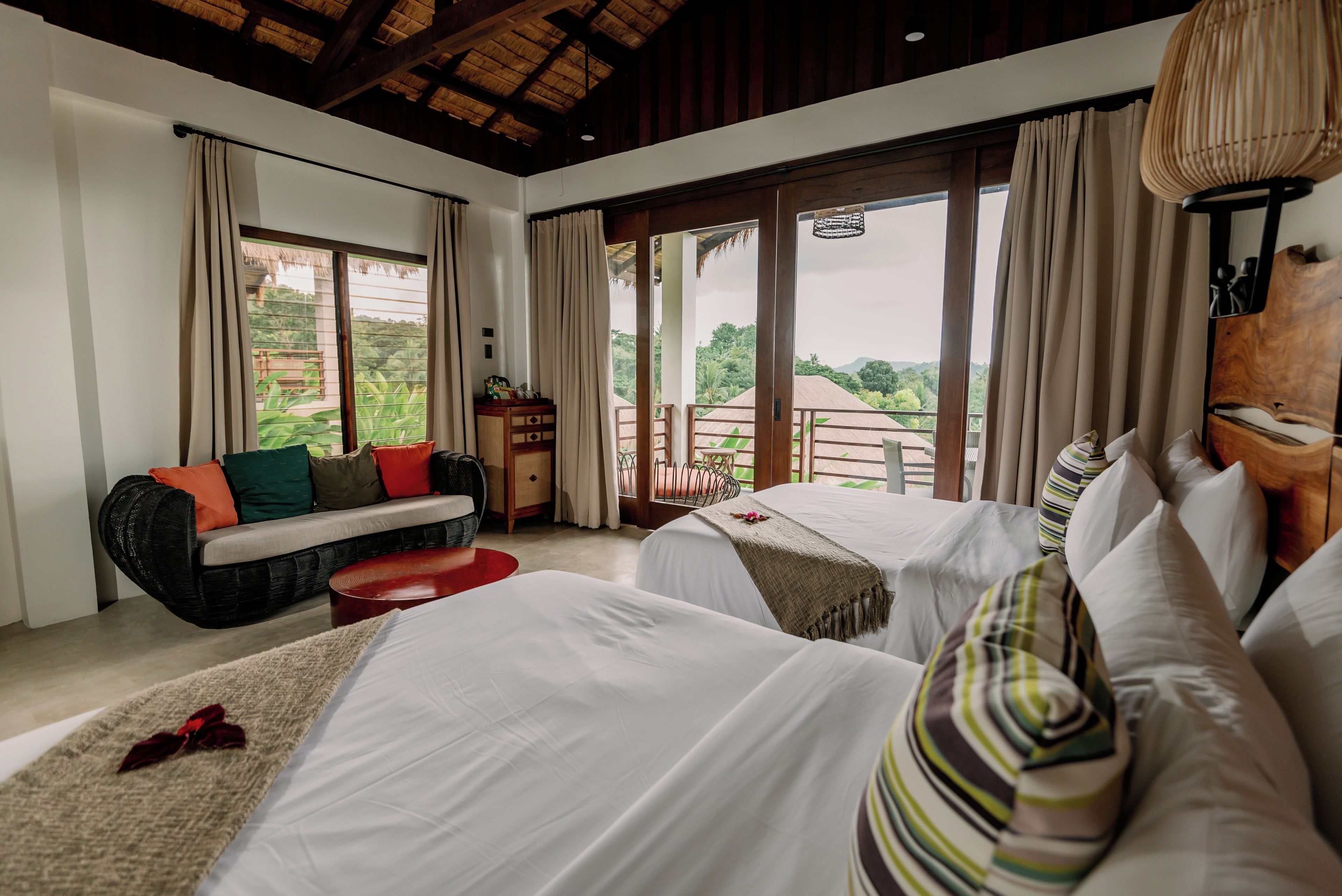 A hotel room with two beds, a sofa, a small table, and a view of the outdoors.