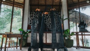 A room with a thatched roof, a hanging light fixture, a zebra-patterned chair, and a view of greenery outside. - La Joya Farm Resort & Spa (Aloguinsan)