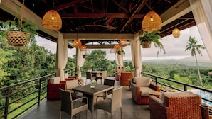An outdoor seating area with wicker furniture, hanging wicker lamps, and a view of lush greenery. - La Joya Farm Resort & Spa (Aloguinsan)
