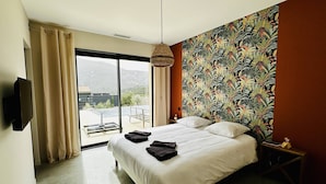 Un dormitorio con una cama grande, un televisor montado en la pared y vistas a una piscina y montañas a través de la ventana.