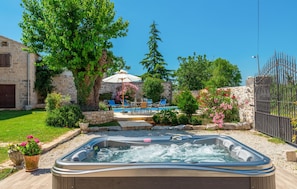 Een bubbelbad in een achtertuin met een stenen muur, een zwembad en tuinmeubilair.