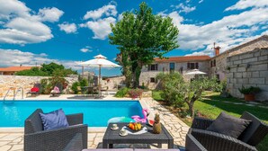 A poolside area with wicker furniture, a table with fruits and a pineapple, and a stone building in the background. - 4 bedroom awesome home in Visnjan (Visnjan)