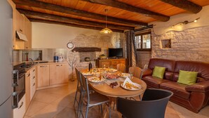 A cozy kitchen with a stone wall, wooden ceiling beams, a dining table set with plates, and a leather sofa with green cushions. - 4 bedroom awesome home in Visnjan (Visnjan)