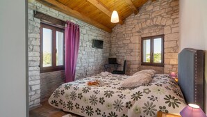 A bedroom with a stone wall, a bed with floral bedding, a laptop on a desk, and a window with curtains. - 4 bedroom awesome home in Visnjan (Visnjan)