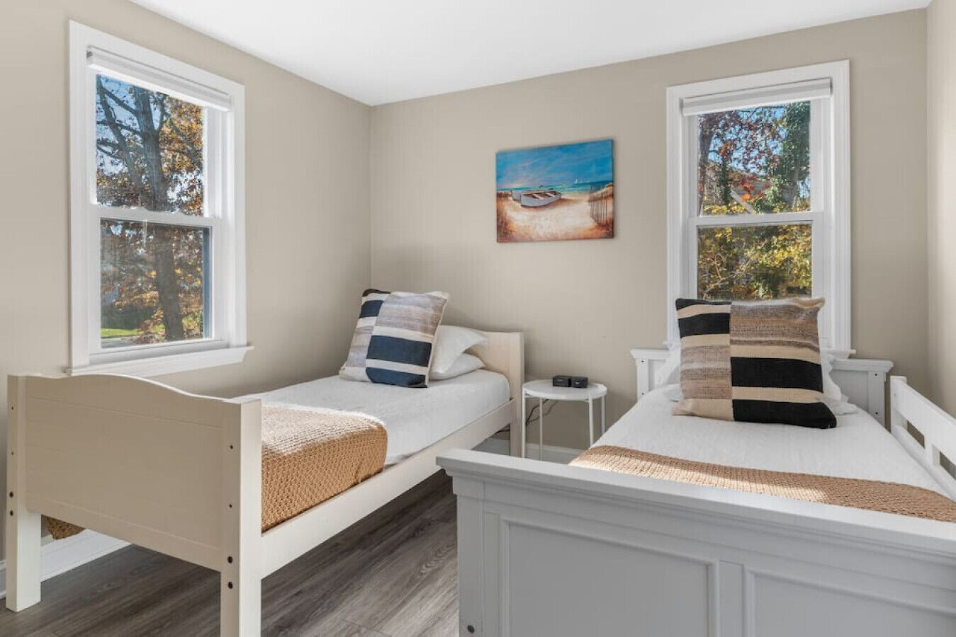 Une chambre avec deux lits simples, une petite table de chevet, une commode et un tableau au mur.