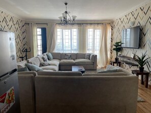 A living room with a sofa, a coffee table, a TV, and a refrigerator. - Ruaka view (Ruaka)