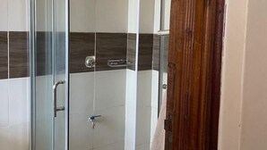 A glass-enclosed shower stall with a handheld showerhead, a towel rack, and a tiled floor. - Ruaka view (Ruaka)