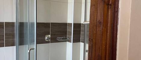 A glass-enclosed shower stall with a handheld showerhead, a towel rack, and a tiled floor.