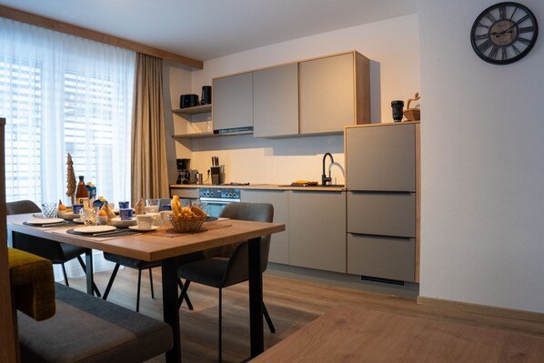 Een moderne keuken met een eettafel gedekt voor twee personen, een inbouwoven en een koelkast.