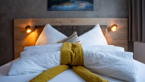 A neatly made bed with white linens and a yellow throw blanket, wooden headboard, and two wall-mounted lights.