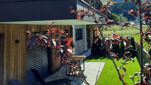 A modern two-story building with a balcony, a patio area with outdoor furniture, and a well-maintained lawn.