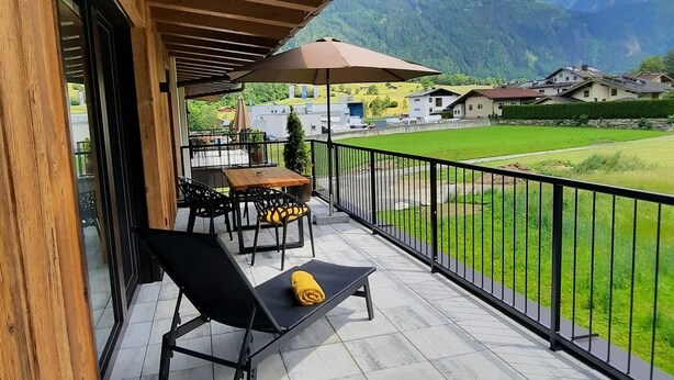 A covered outdoor area with a table and chairs, a yellow towel, and a view of a green landscape and mountains.