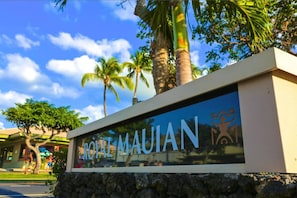 A sign with 'ROYAL MAUIAN' written on it, surrounded by palm trees and a clear sky.