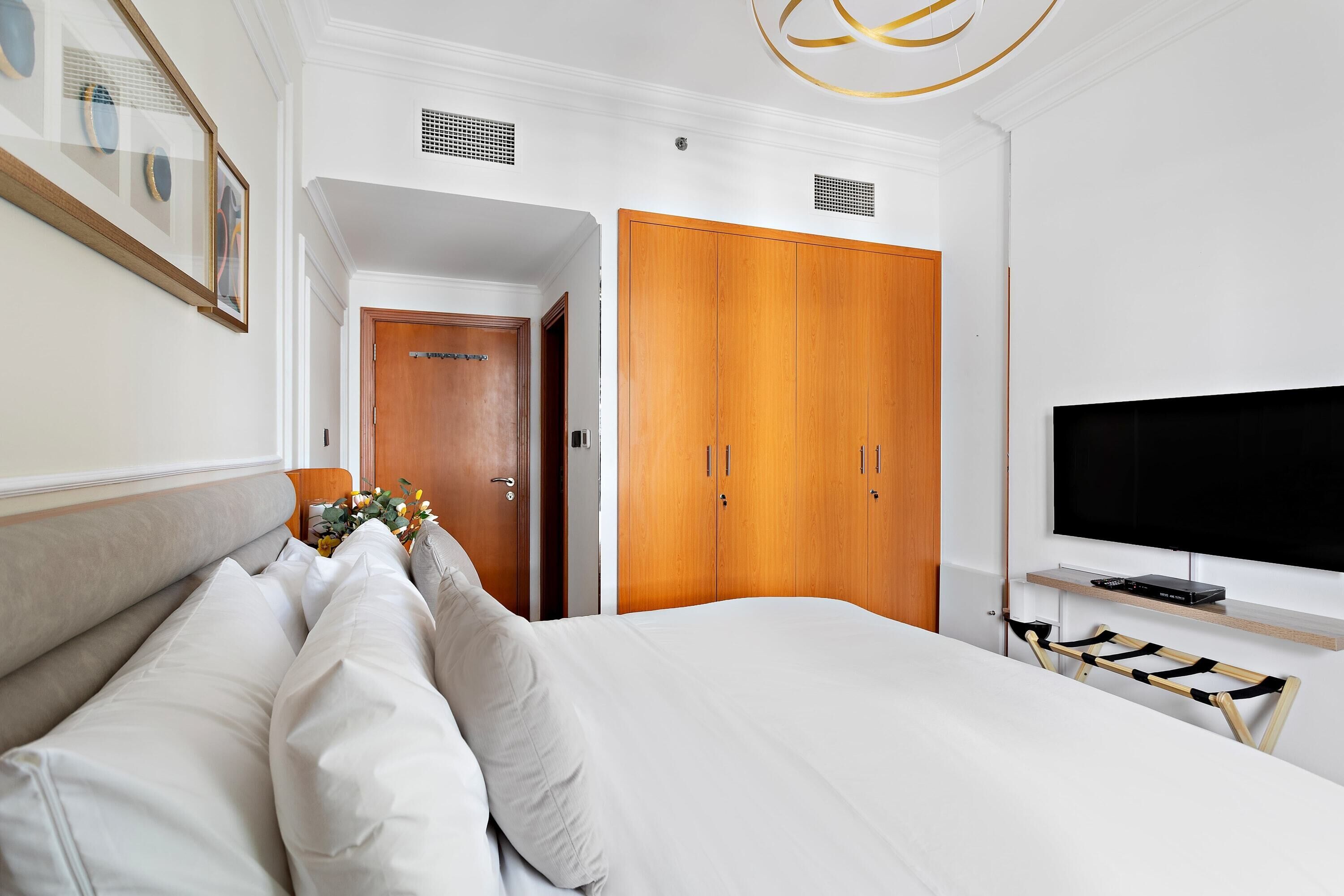 A hotel room with a large bed, wooden wardrobe, a television, and a small table with a decorative item.