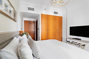 A hotel room with a large bed, wooden wardrobe, a television, and a small table with a decorative item. - Silkhaus Manchester Tower, Dubai Marina (Dubai)