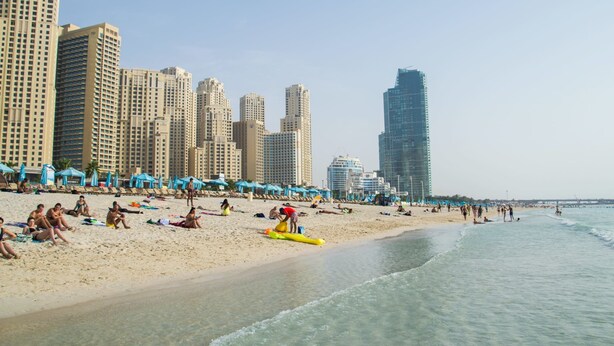 A beach with high-rise buildings in the background, sandy beach, and people relaxing. - Silkhaus Manchester Tower, Dubai Marina (Dubai)