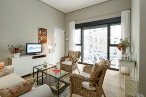 Uma sala de estar moderna com televisão de tela plana, cadeiras de vime, uma mesa de centro de vidro e vista através de uma janela ampla.