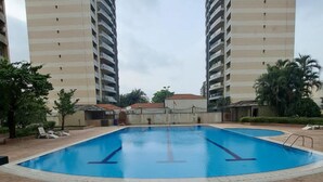 En swimmingpool omgiven av en gångväg av tegelstenar, med två höga byggnader i bakgrunden.