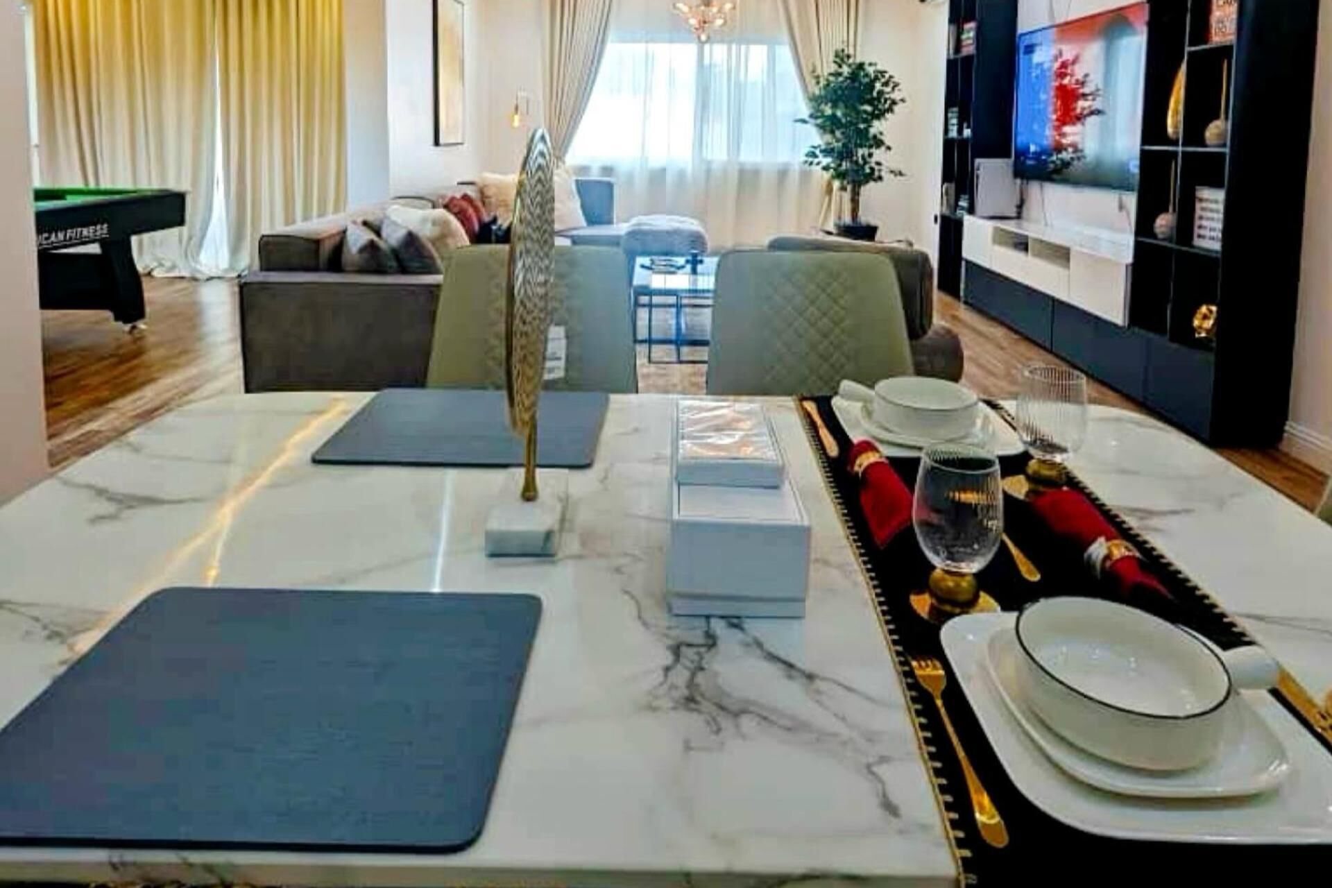 Un salon moderne avec une table basse en marbre, un tapis de yoga et une table à manger dressée avec des assiettes, des verres et des couverts.