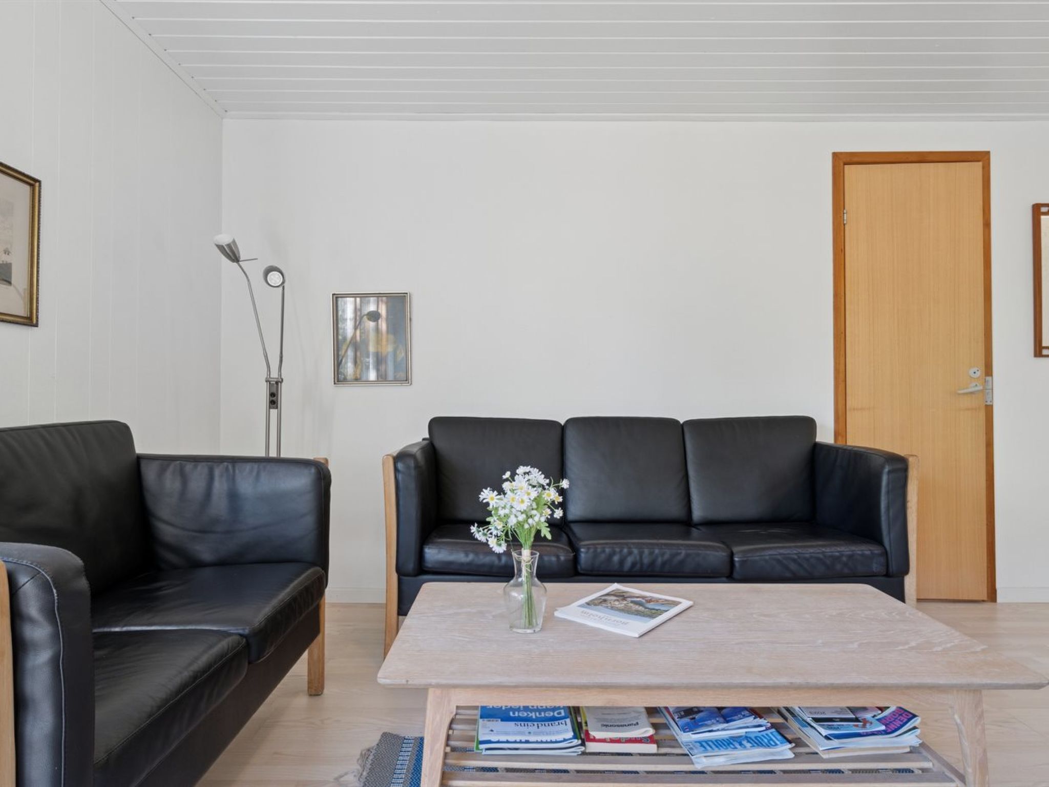 Un salon avec un canapé en cuir noir, une table basse avec des magazines et un vase rempli de fleurs.