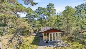 A small cabin with a red roof and glass walls, surrounded by dense forest.