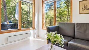 A modern living room with a leather sofa, a vase with flowers, and large windows with wooden frames.
