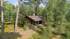 Metsän keskellä sijaitseva mökki, jossa on pieni kuisti ja savupiippu.