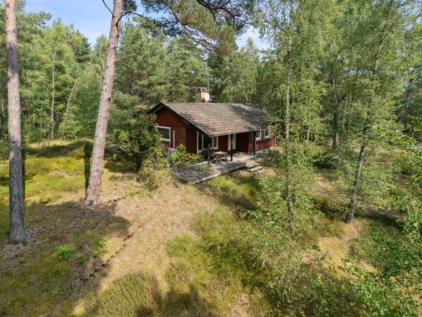 Eine Hütte, umgeben von dichtem Wald, mit einer kleinen Veranda und einem Schornstein.