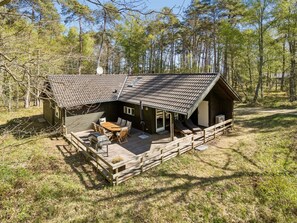 Uma cabana com telhado inclinado, um deck com móveis externos e um pátio cercado.