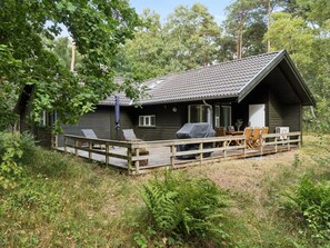 A cabin with a deck, outdoor seating, and a covered grill area.
