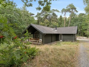 A cabin with a sloped roof, a porch with seating, and a gravel driveway.