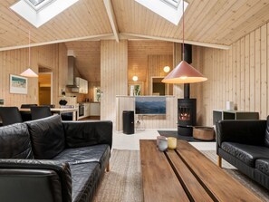 A spacious living area with a high ceiling, wooden walls, a fireplace, and a television.