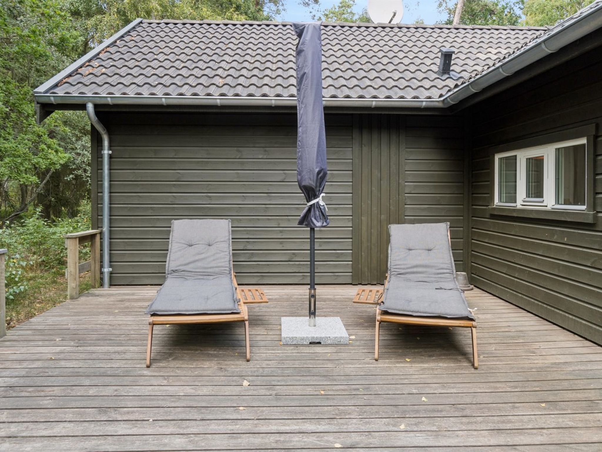A wooden deck with two lounge chairs and a covered umbrella.