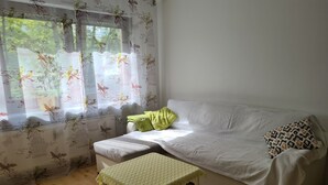 Um quarto aconchegante com um sofá branco, uma mesa pequena com toalha xadrez, um travesseiro verde e um travesseiro com estampa de leopardo.