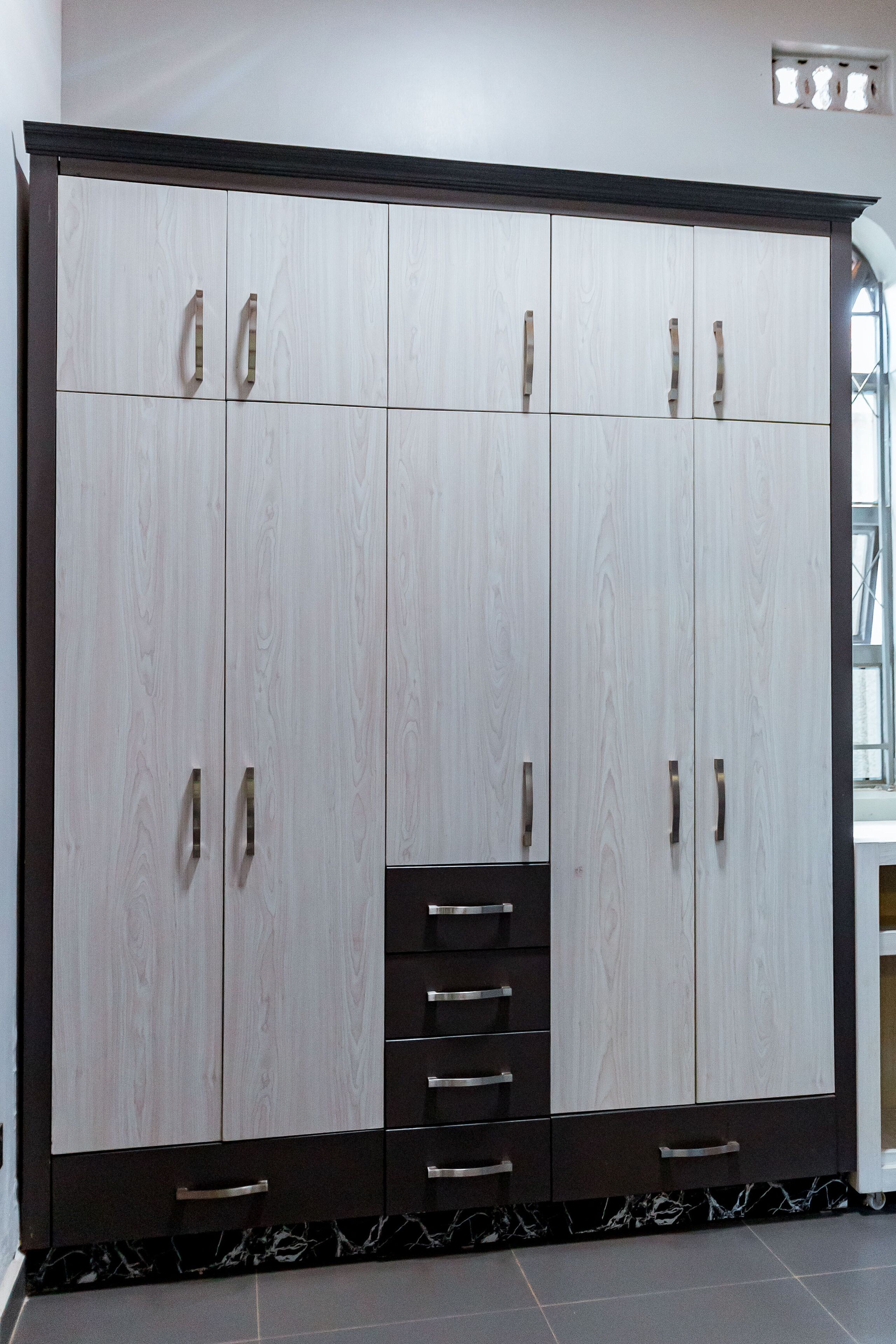 A large wardrobe with multiple compartments and drawers, featuring a dark base and lighter upper sections.