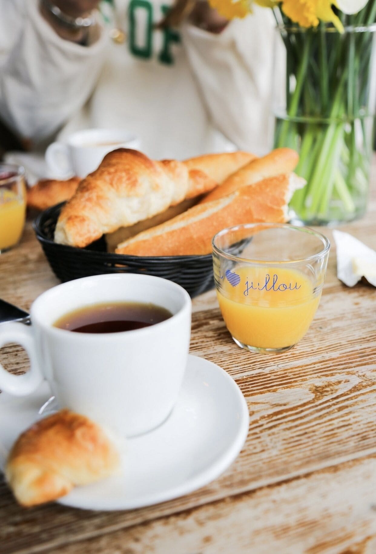 Une table en bois dressée pour le petit-déjeuner, avec des croissants, une tasse de café et un verre de jus d’orange.