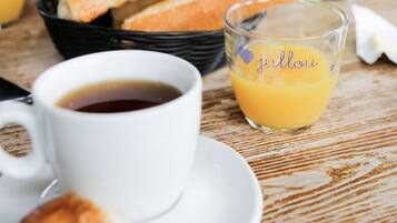 Un desayuno con cruasanes, una taza de café y un vaso de jugo de naranja sobre una mesa de madera.
