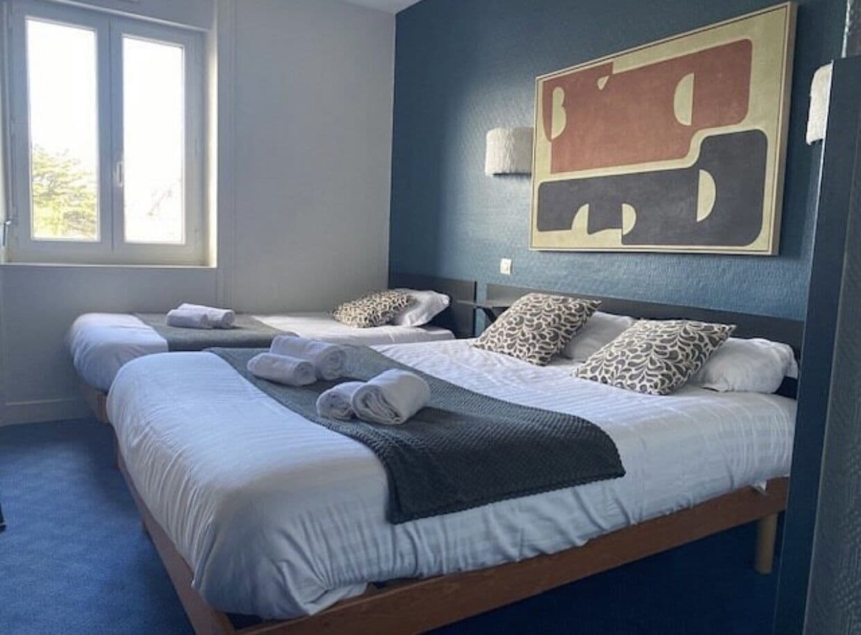 A hotel room with two beds, a large abstract painting on the wall, and a window with daylight.