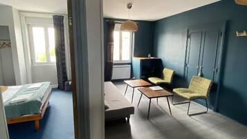 A room with a bed, a sofa, a small table, and a chair. There is a window with curtains and a door.