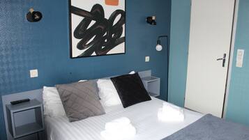 Une chambre d’hôtel comprenant un lit, une table de chevet, une œuvre d’art accrochée au mur, une porte et une prise électrique.