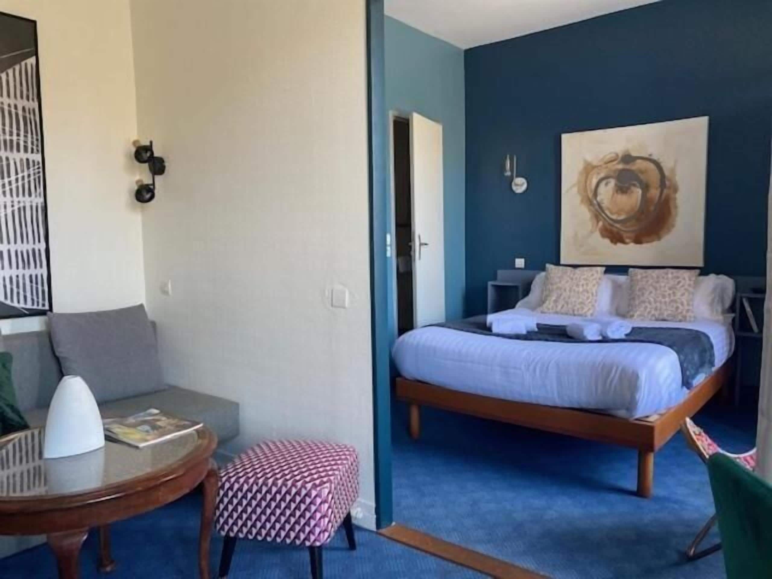 Une chambre à coucher avec un lit, une petite table ronde, une chaise et un tableau accroché au mur.