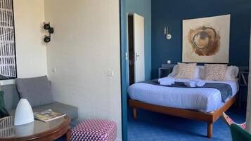 Une chambre à coucher avec un lit, une petite table ronde, une chaise et un tableau accroché au mur.