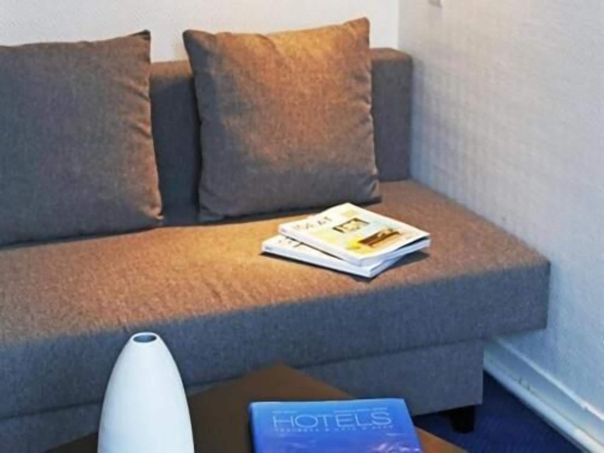 Um sofá com uma revista e um livro em cima, e um vaso branco sobre uma mesinha de apoio.