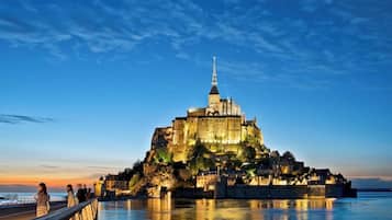 A historic castle with a prominent tower, situated on a rocky island with a waterfront promenade.